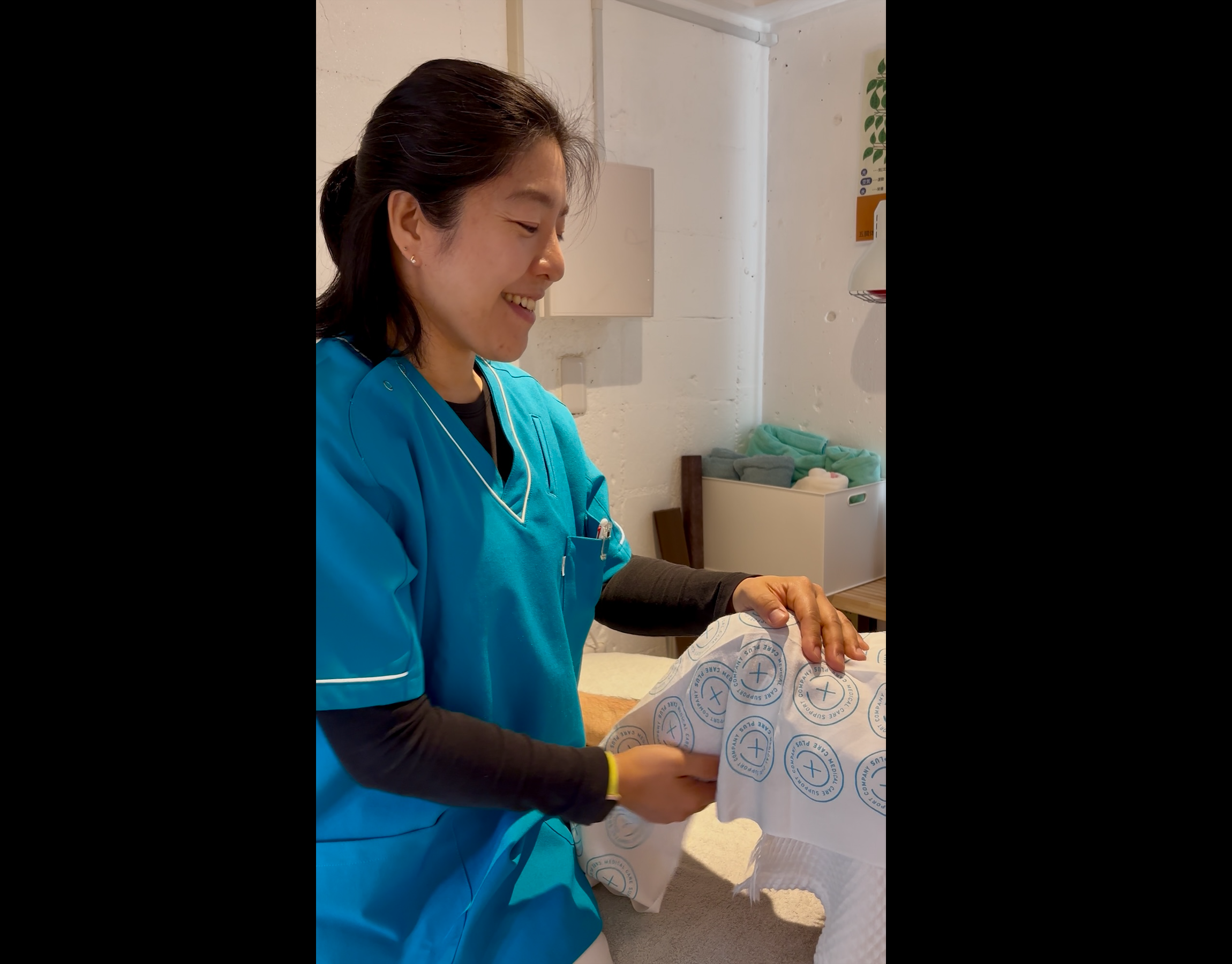 A healthcare worker in blue scrubs smiles while handling medical packaging materials at a table