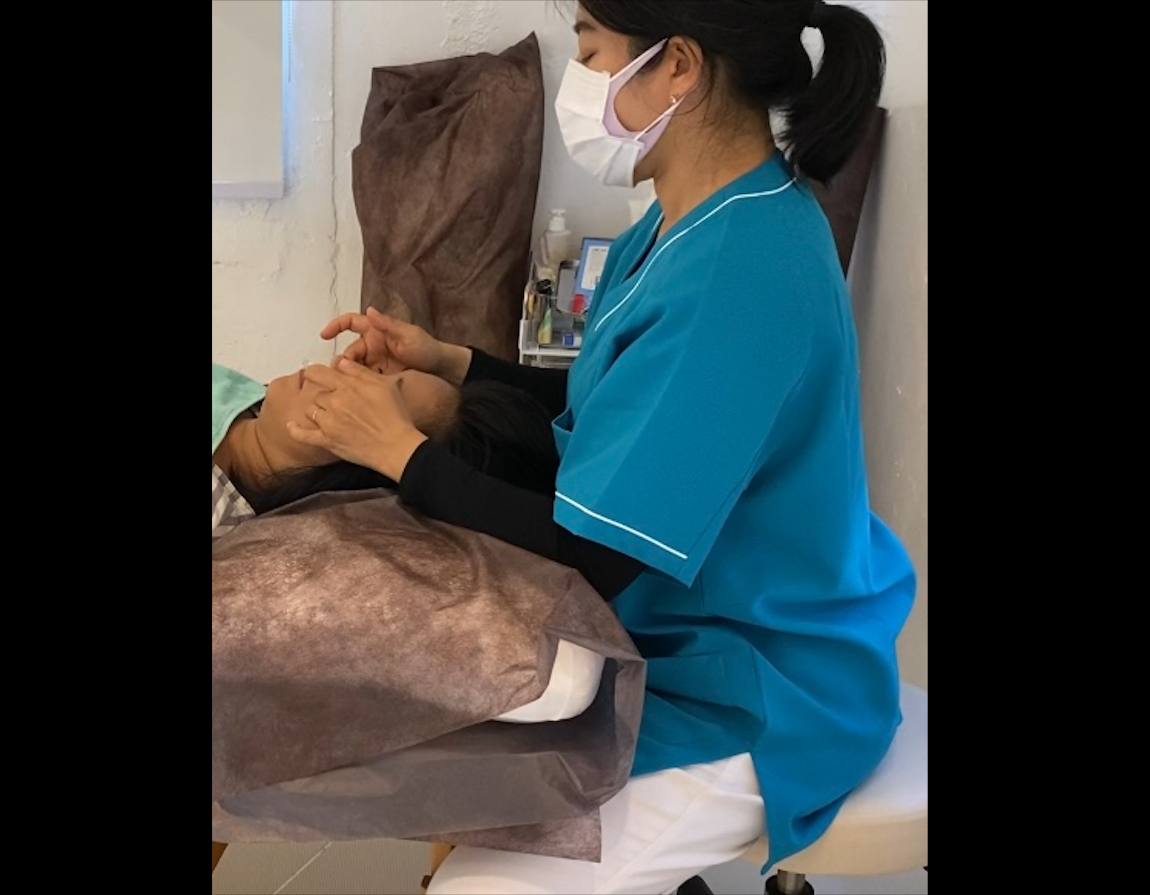 Healthcare worker in blue scrubs and mask examining patient's leg during medical examination