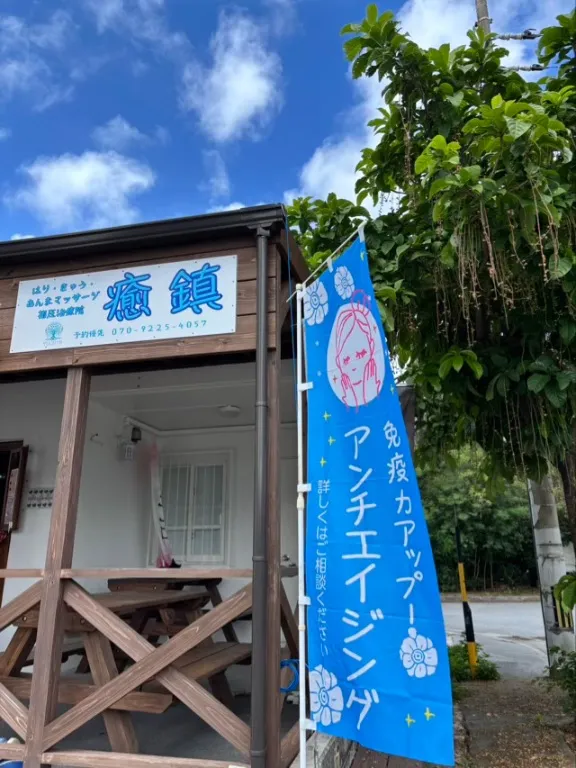 Small Japanese restaurant shop with wooden storefront, blue signage, and lush green vegetation overhead