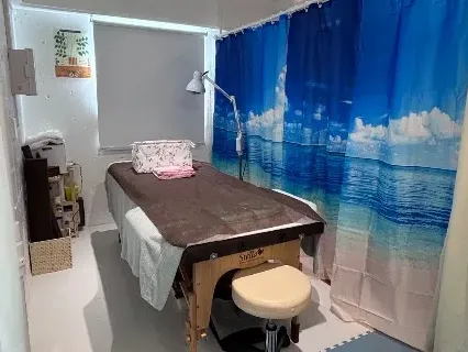 Massage therapy room with treatment table, stool, blue ocean curtain, and supplies